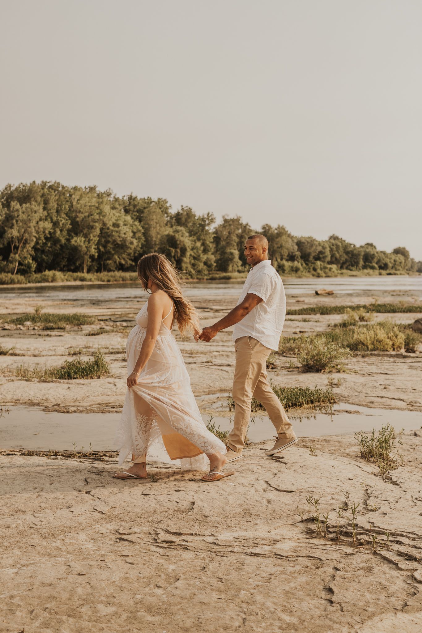 Couple playfully dances together on sandy terrain during sunset photoshoot.