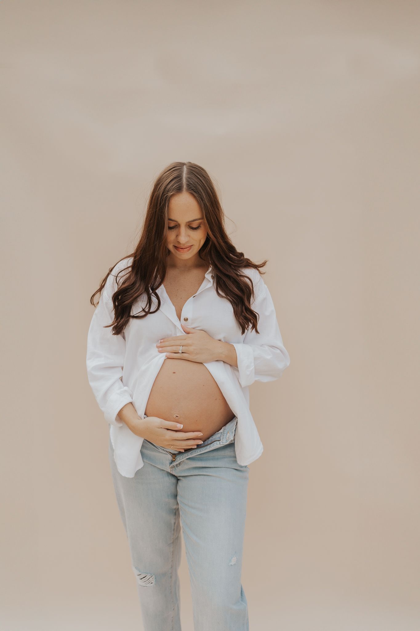 Studio maternity photo series showing a pregnant woman in a white shirt and jeans against a neutral background in Michigan.