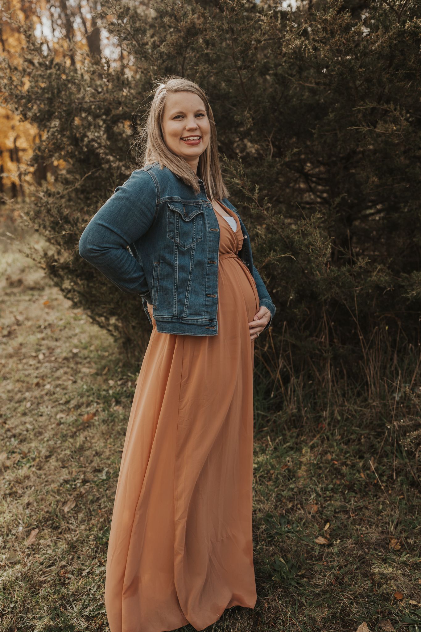 Autumn maternity photos featuring a rust-colored dress and denim jacket outdoors.