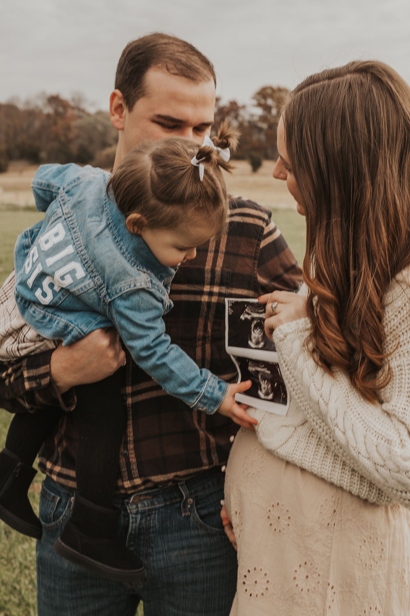 Joyful family moment captured outdoors while holding ultrasound photo during pregnancy announcement.
