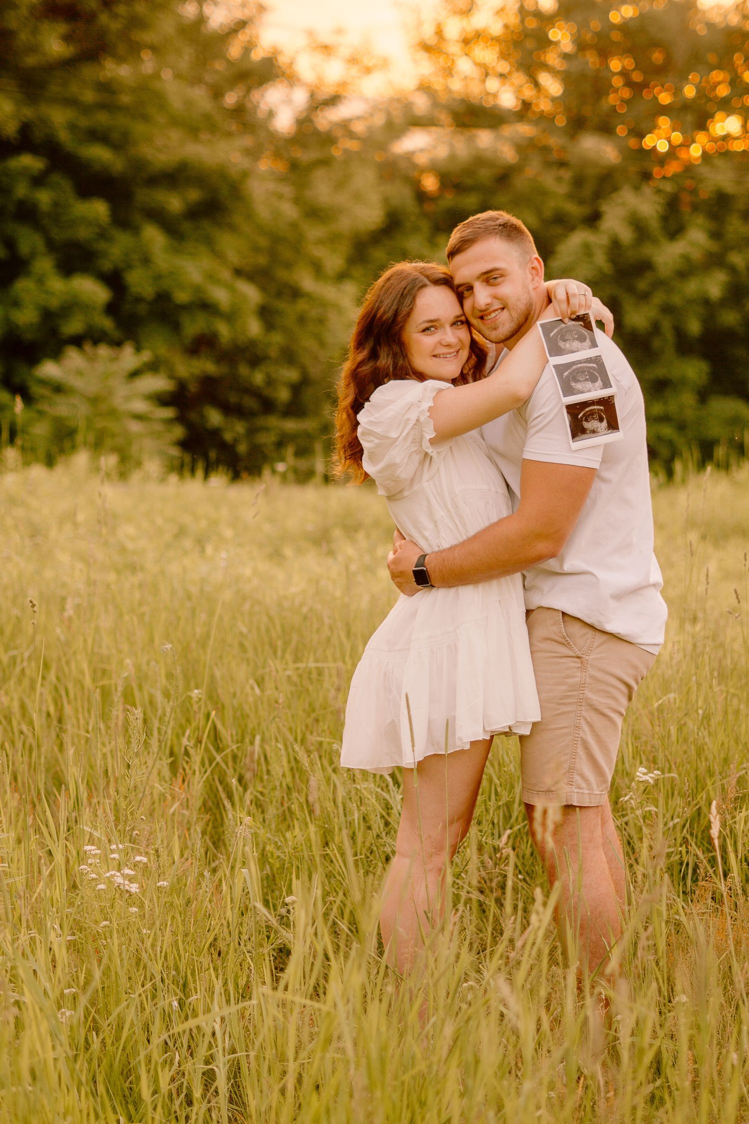Couple sharing intimate moment in tall grass field during golden hour sunset.