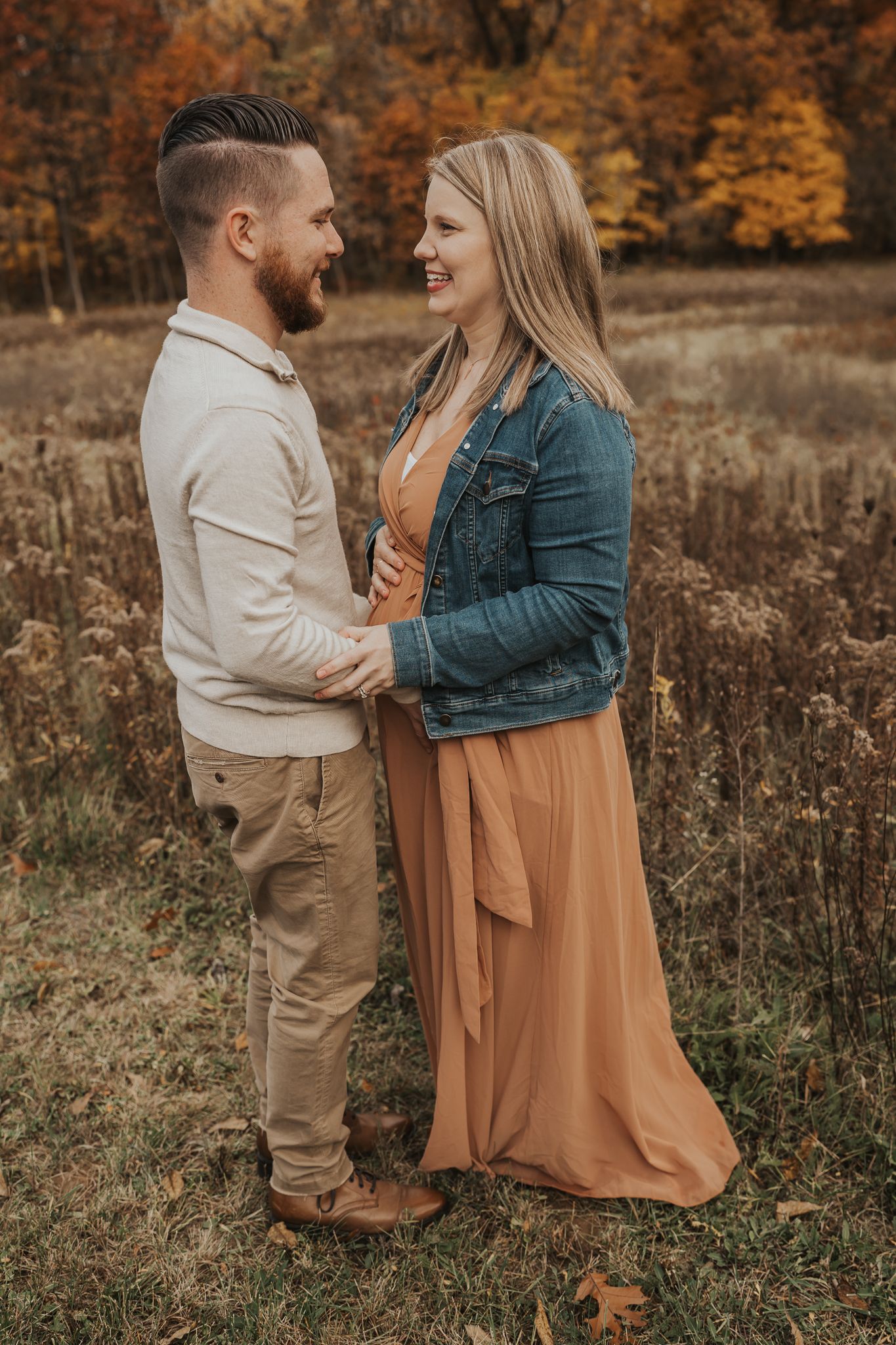 Candid maternity photos of couple laughing together in fall field setting.
