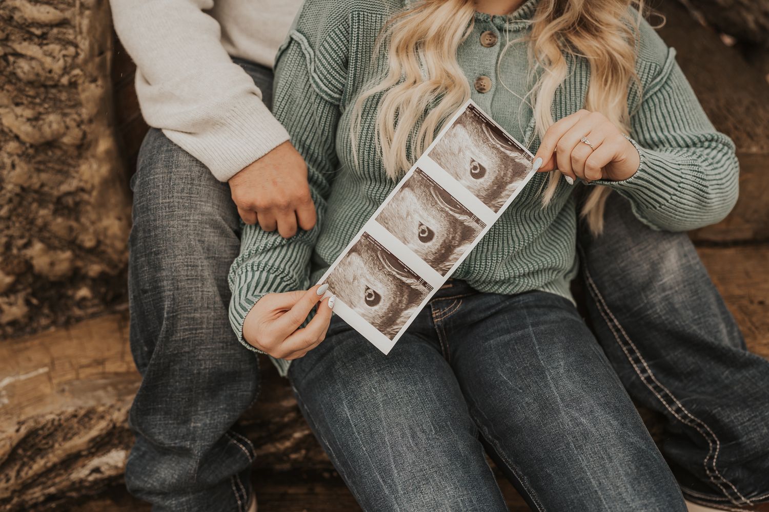 Couple holding ultrasound photos during outdoor pregnancy announcement session.