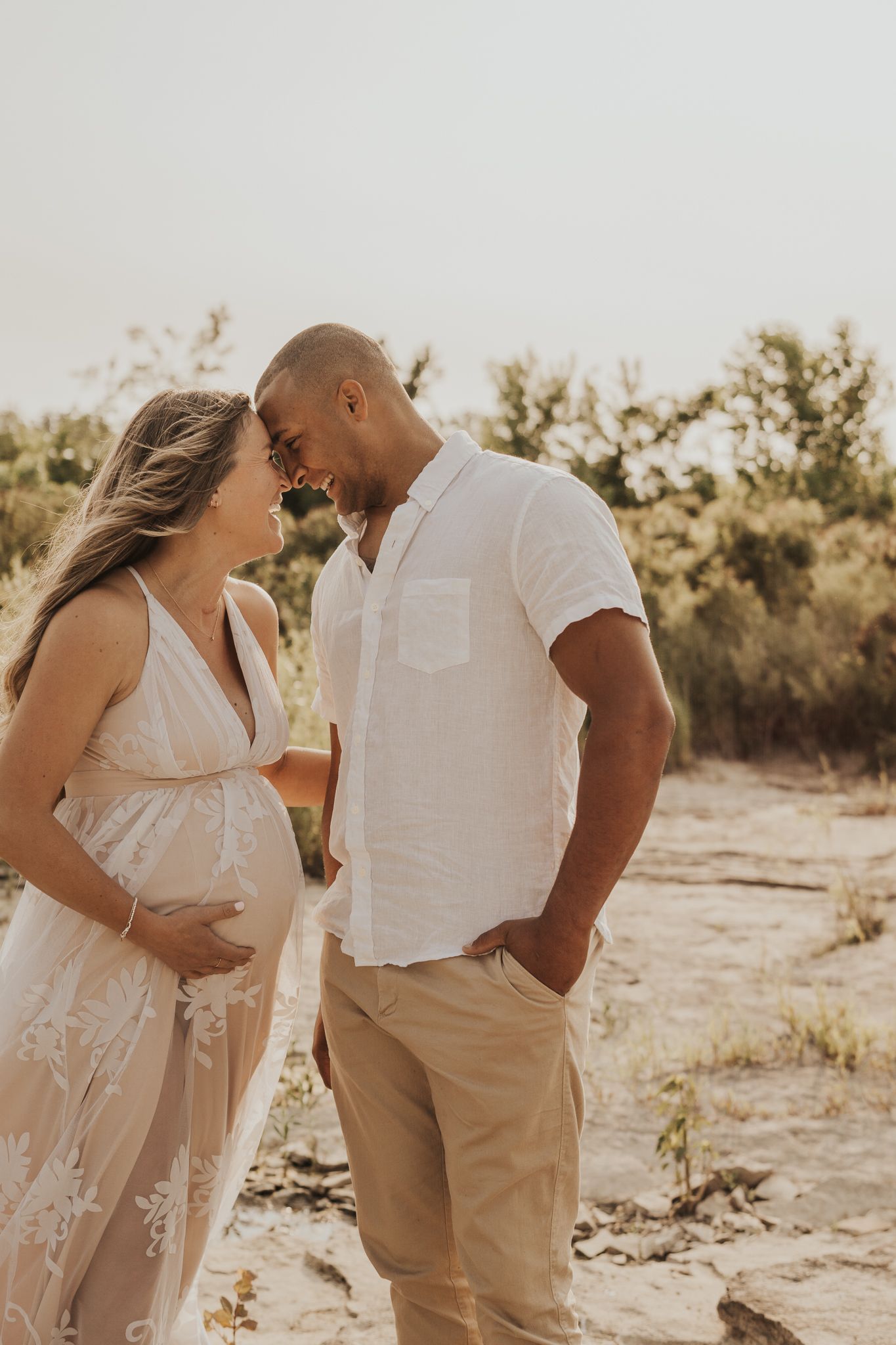 Couple in white and khaki outfits embrace during golden hour desert photoshoot.