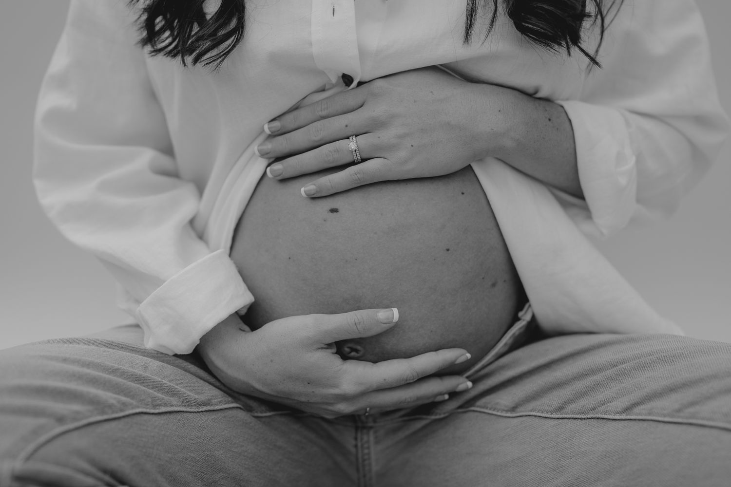 Black and white Michigan studio close-up of hands tenderly cradling pregnant belly.