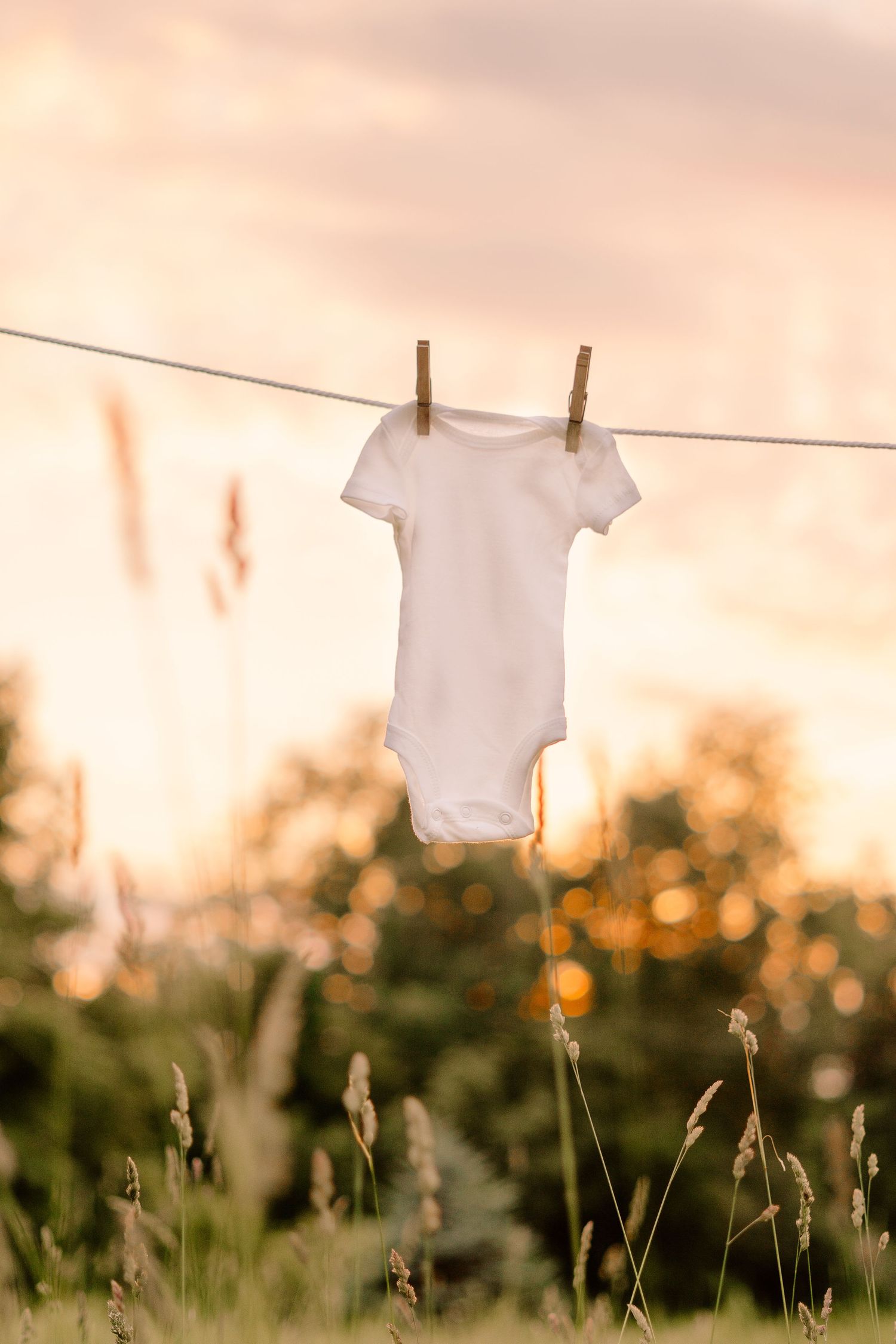 White baby onesie hanging on clothesline at sunset with bokeh background.