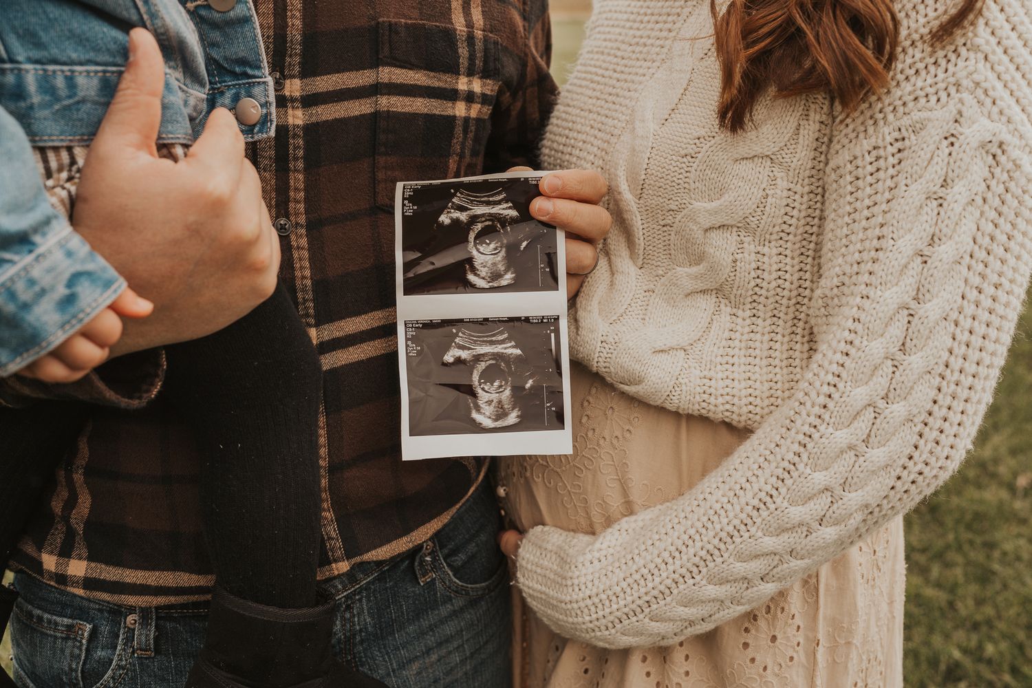 Family holds ultrasound photo near Concord Mi outdoor setting during autumn pregnancy announcement photoshoot.
