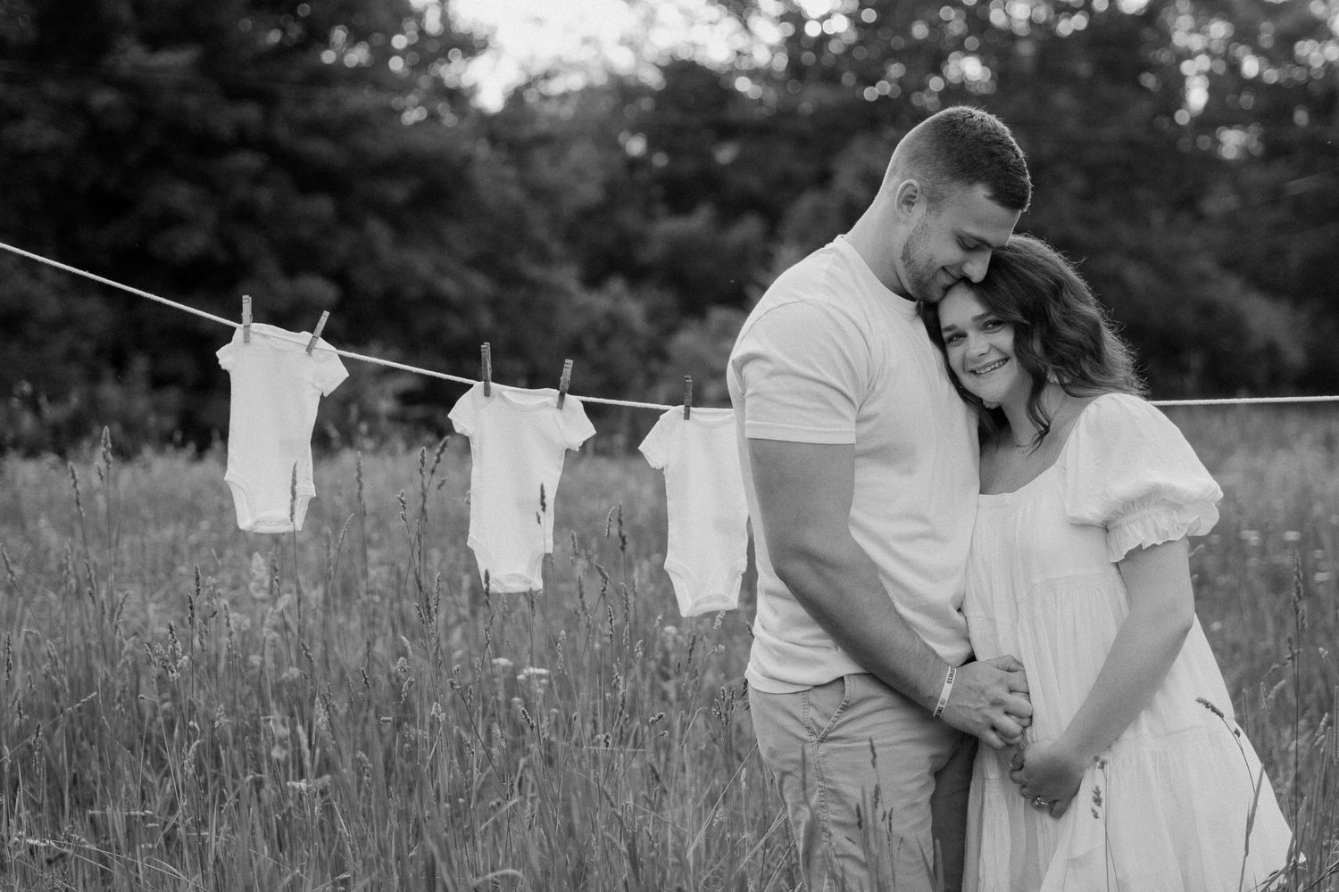 Baby clothes on clothesline with couple embracing in background of a Michigan sunset.