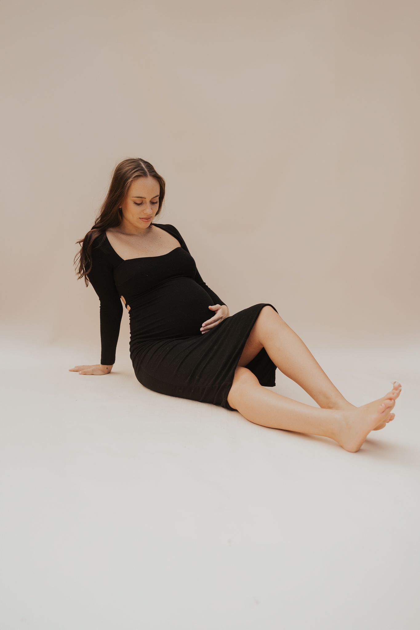 Artistic Michigan studio maternity portrait of pregnant woman in black dress against neutral background.