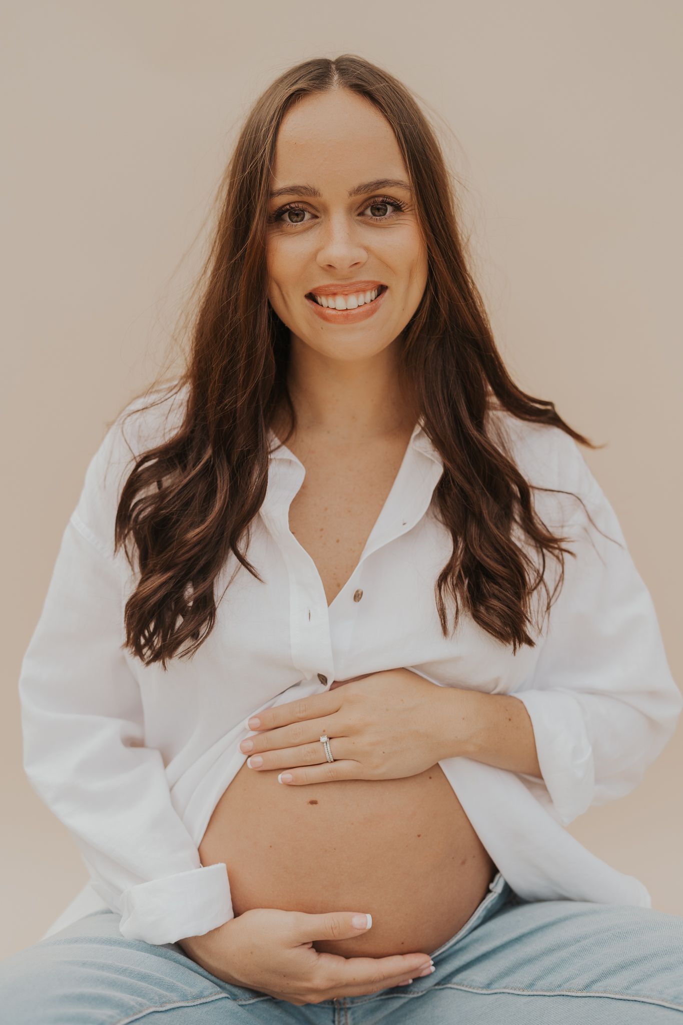 Michigan maternity portrait in white button-down shirt with hands cradling pregnant belly.