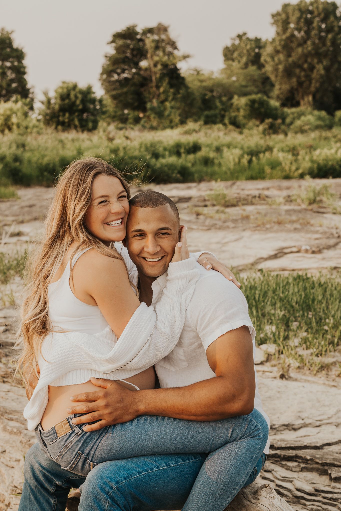 Couple shares intimate moments during outdoor sunset photoshoot on rocky terrain.