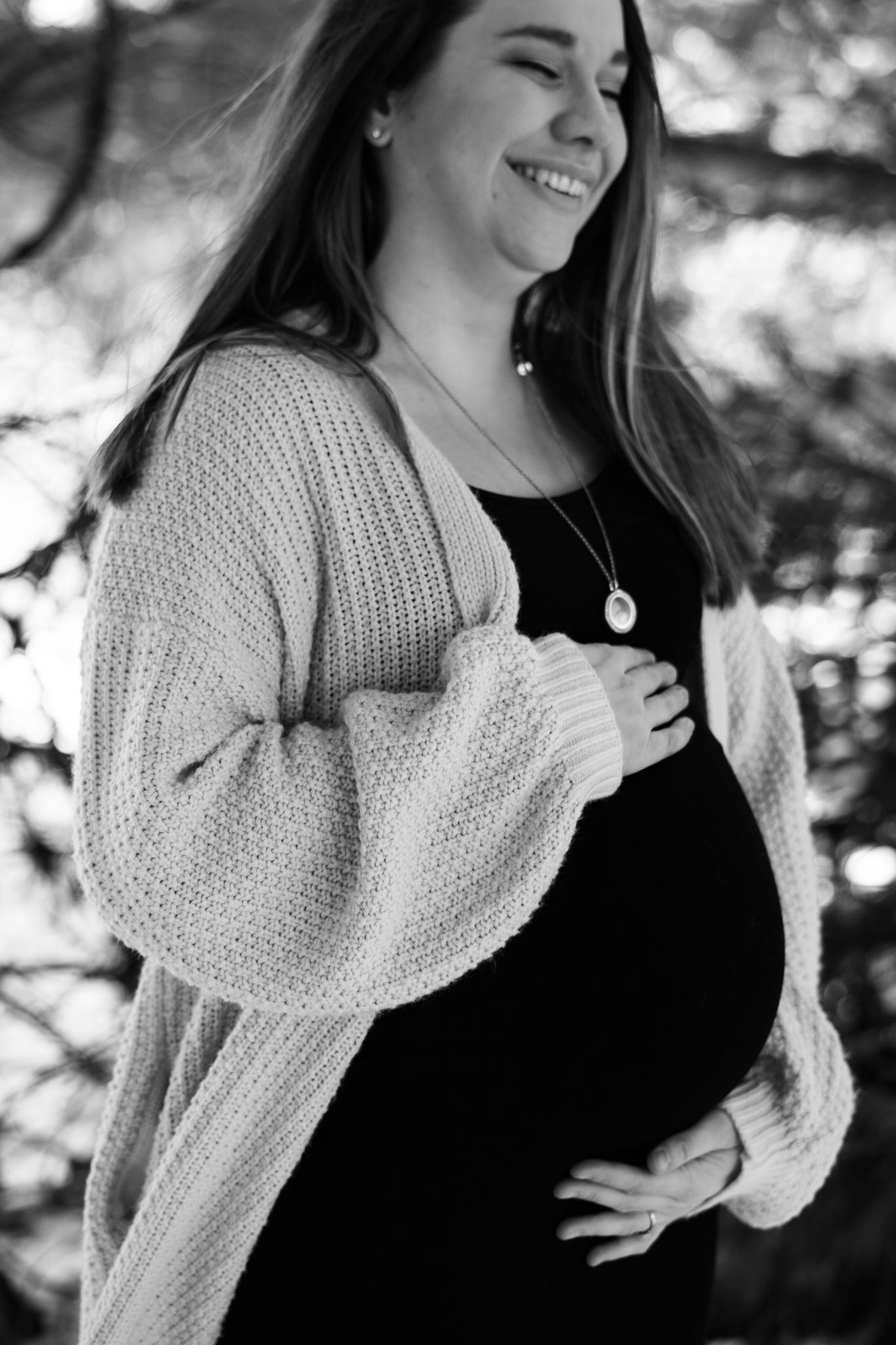 Expectant mother in knit cardigan smiling against winter backdrop.