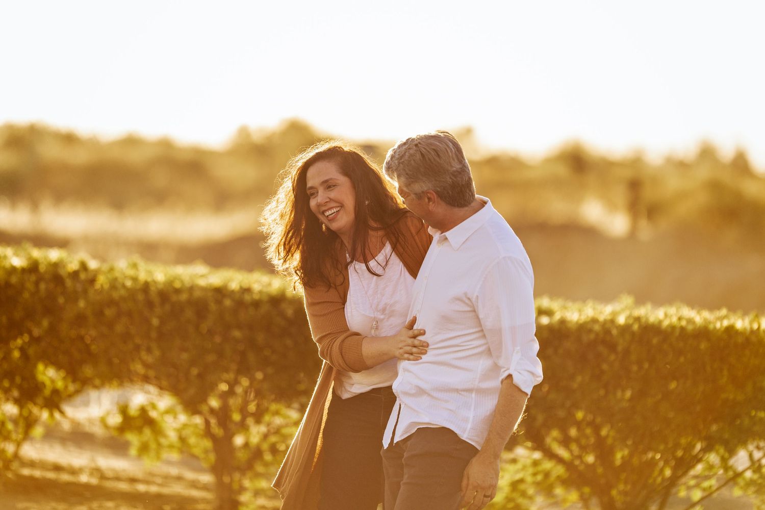 Happy couple embracing and laughing at sunset in a natural outdoor setting.