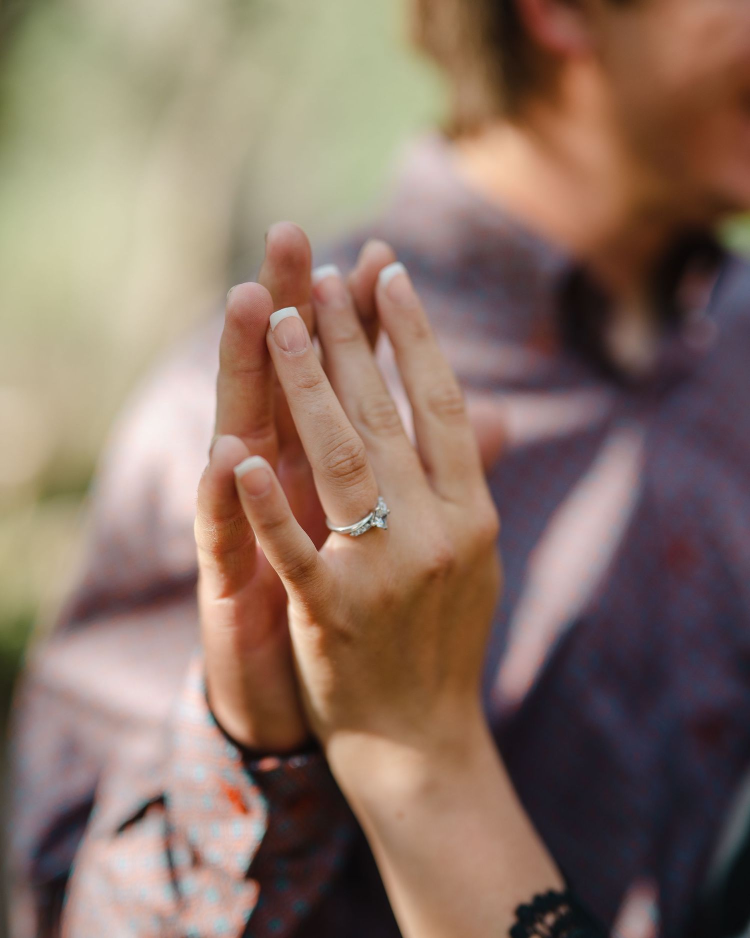 Close-up shot of hands displaying an engagement ring in natural outdoor lighting.