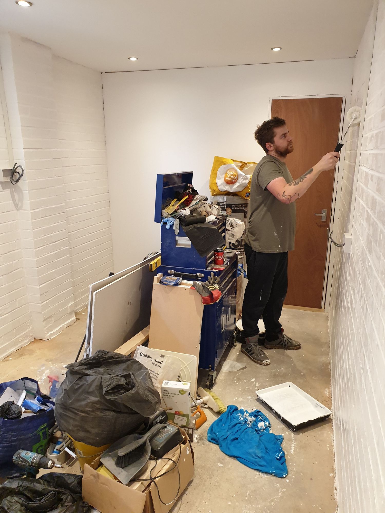 Room renovation in progress with tools and boxes scattered on floor near painted white brick walls.