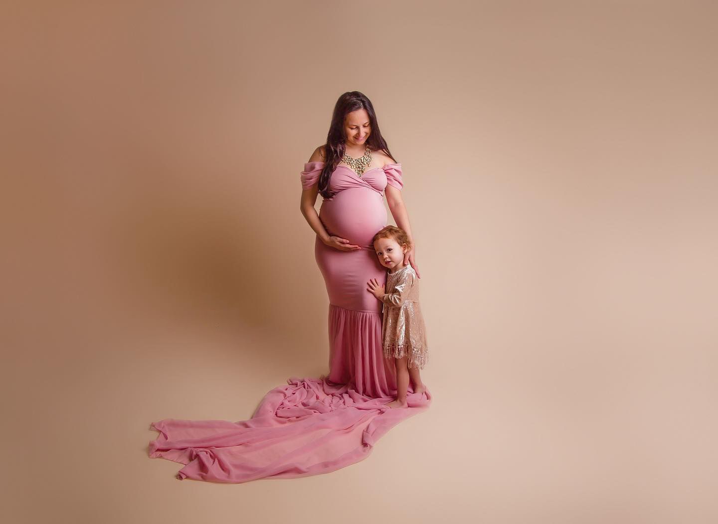 Studio maternity portrait in pink dress with flowing train.