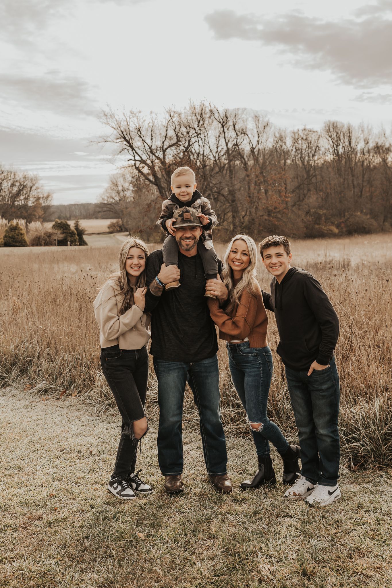 A family group poses together in coordinated outfits on a grassy field during golden hour.