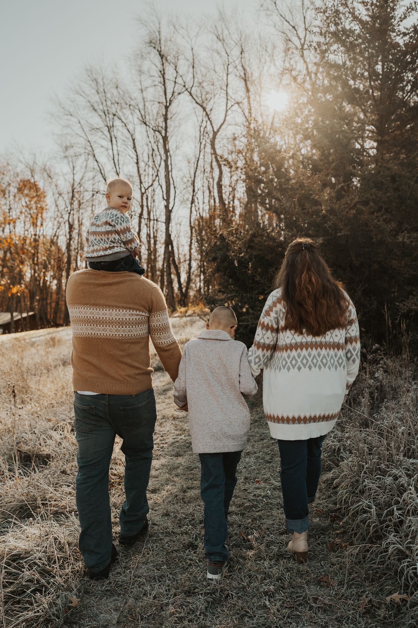 Four people in cozy winter sweaters walk away from camera during golden hour.