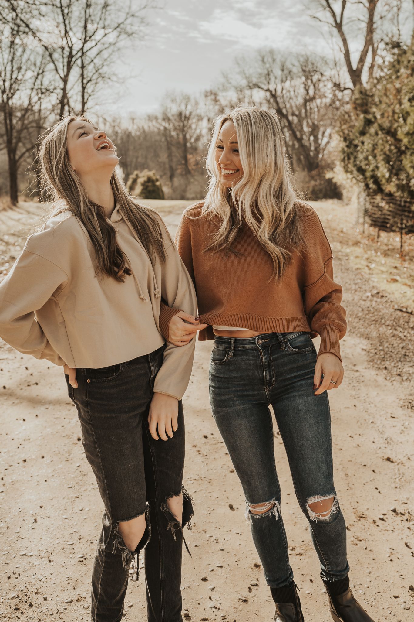 Family in casual sweaters and ripped jeans share laughs while posing on a fall path in Michigan.