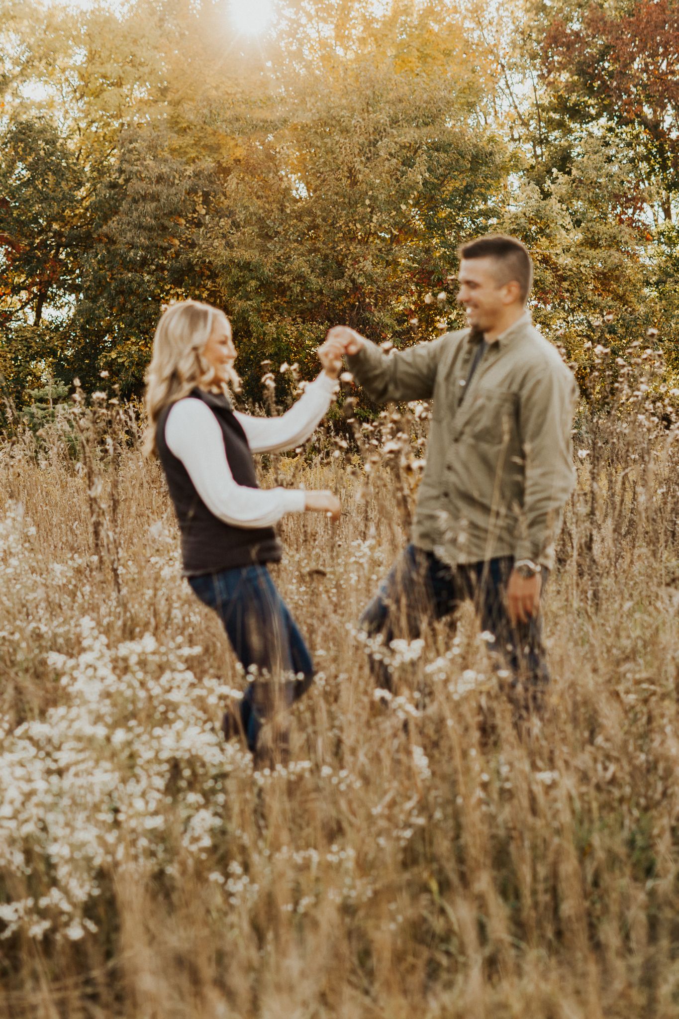 Playful couple dancing and twirling through tall grass in warm autumn sunlight.