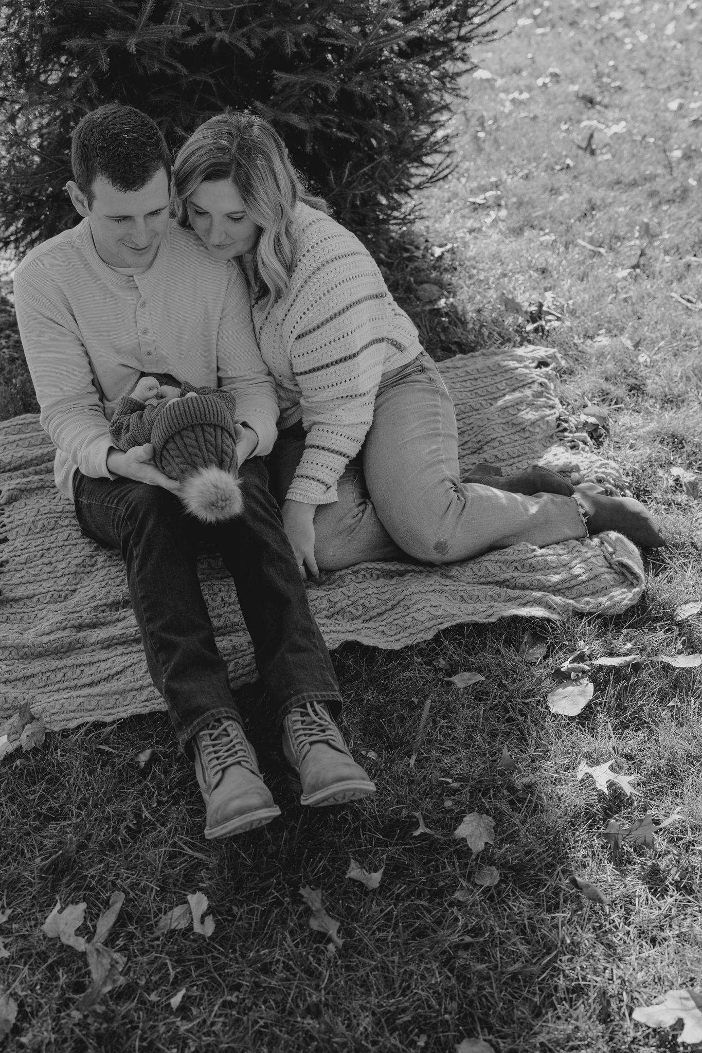 A couple relaxes on a blanket outdoors during a casual newborn photo session.