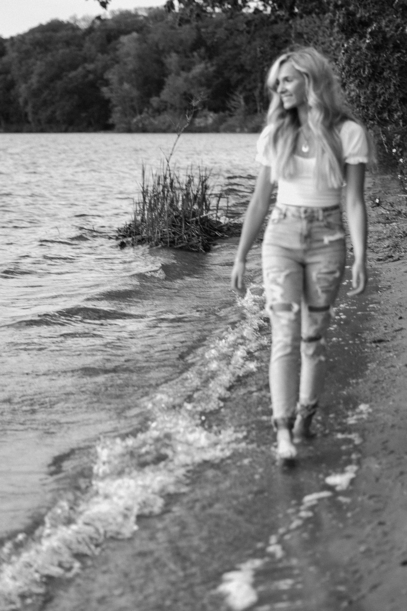 Person walking along a shoreline creating splashes in shallow water.