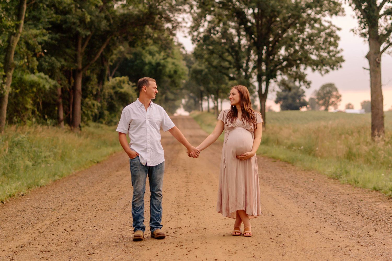 Maternity photos taken down a Michigan tree-lined dirt path at sunset.