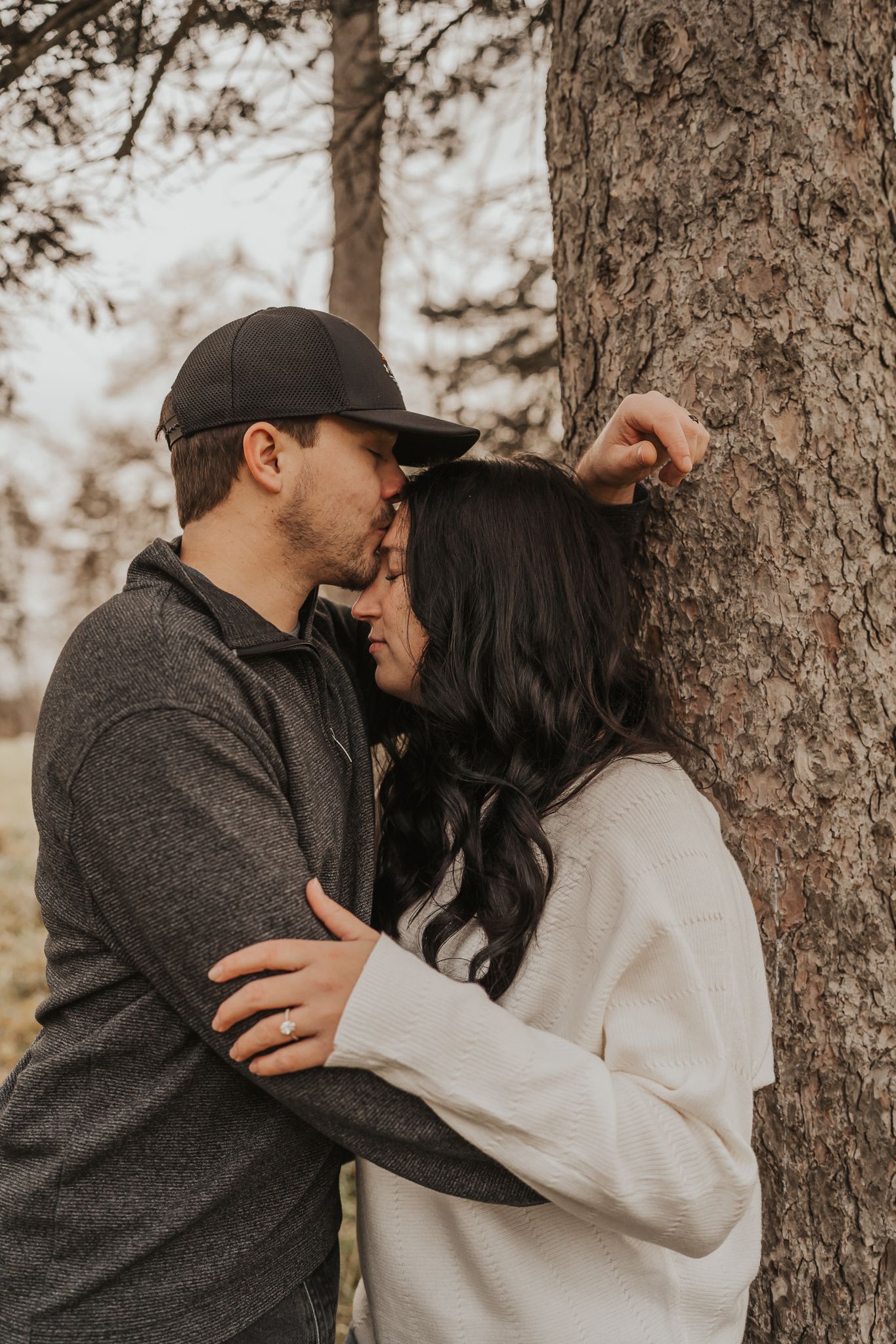 Intimate moment between couple embracing near pine tree in casual winter clothing.