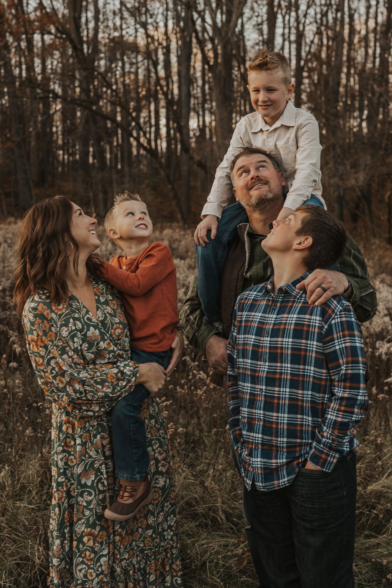A family shares playful moments in plaid and floral outfits among autumn foliage.