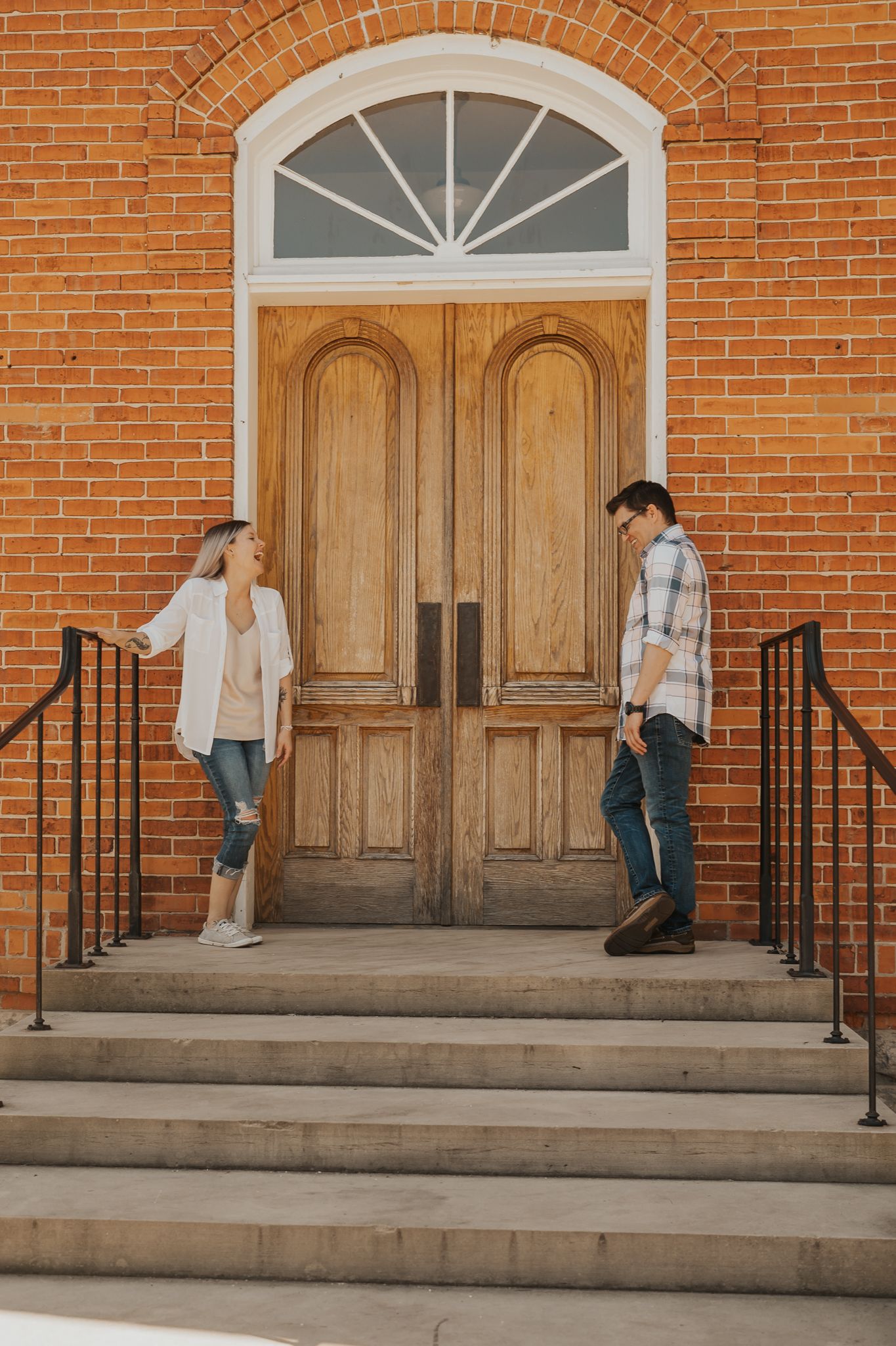 Couple kneeling and proposing on brick church steps with wooden doors in the background.