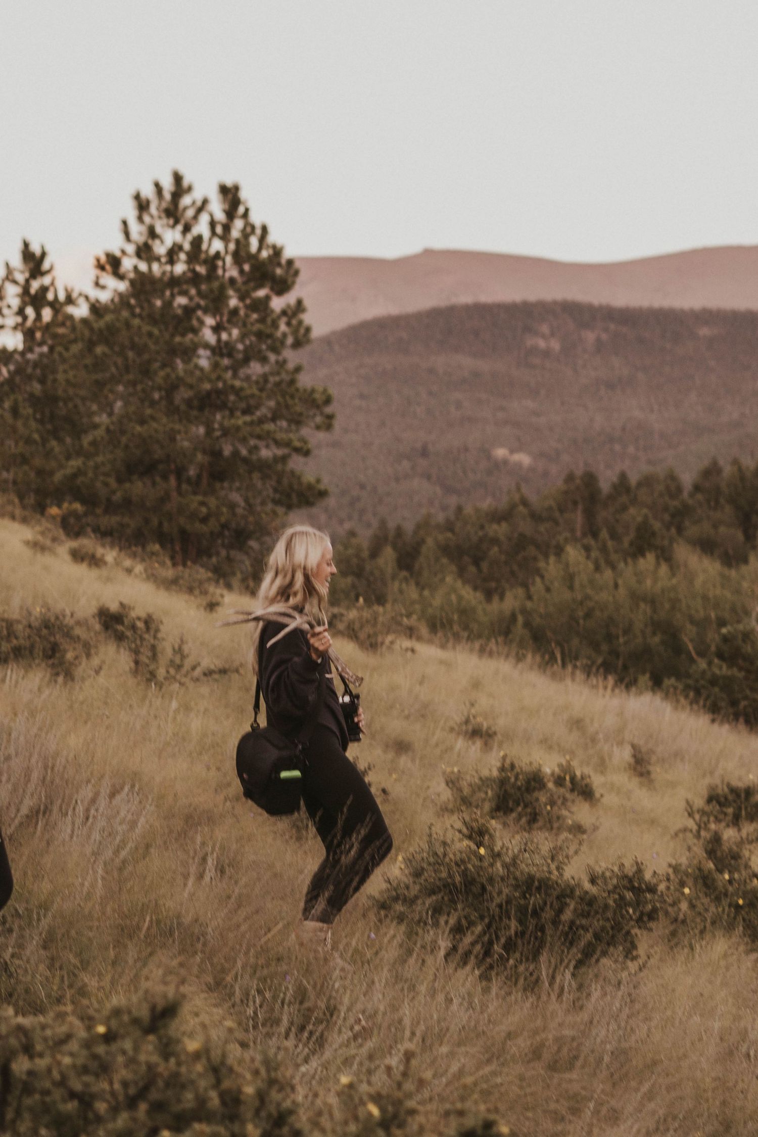 Adventurer hiking through tall grass on a mountainside during golden hour.