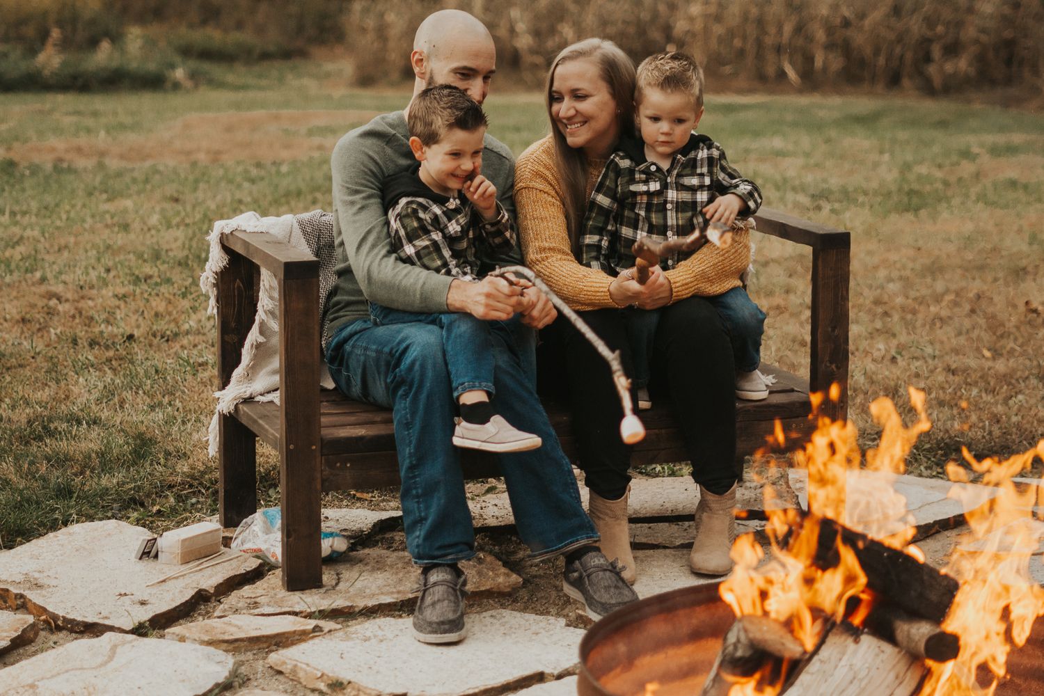 Family enjoying quality time together on bench near warm fire pit outdoors.