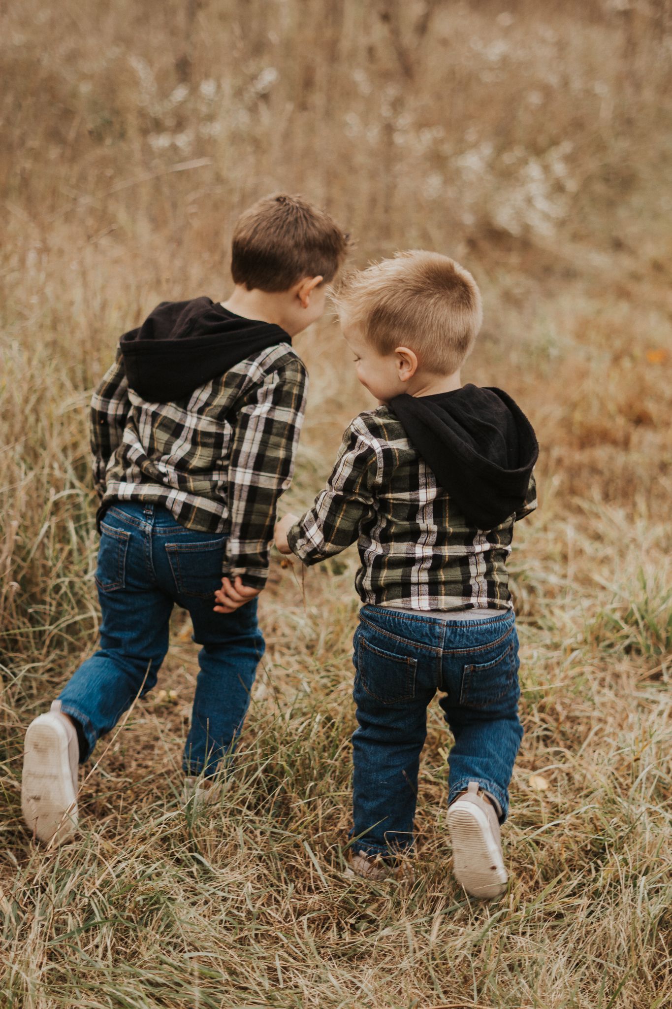 Young children playing and exploring in tall grass wearing plaid shirts and jeans.