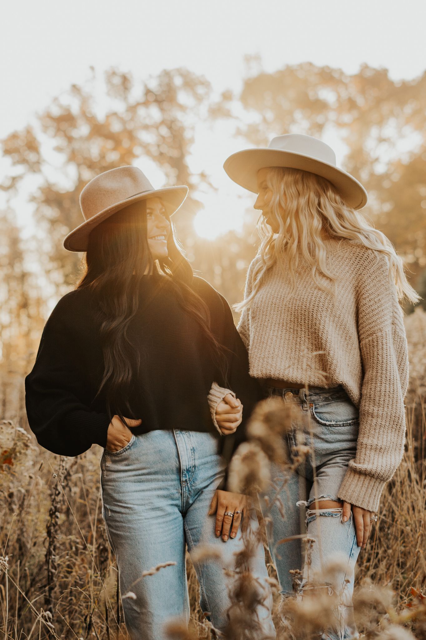 People wearing cozy sweaters and hats stand together in a sunlit autumn field.