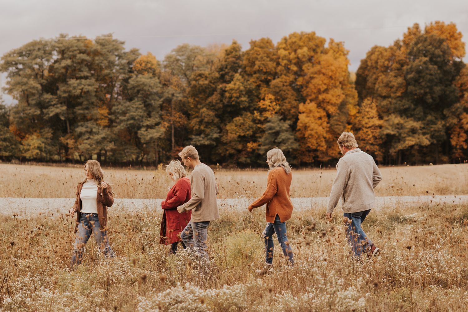 Group walking through golden autumn field with fall foliage in background.