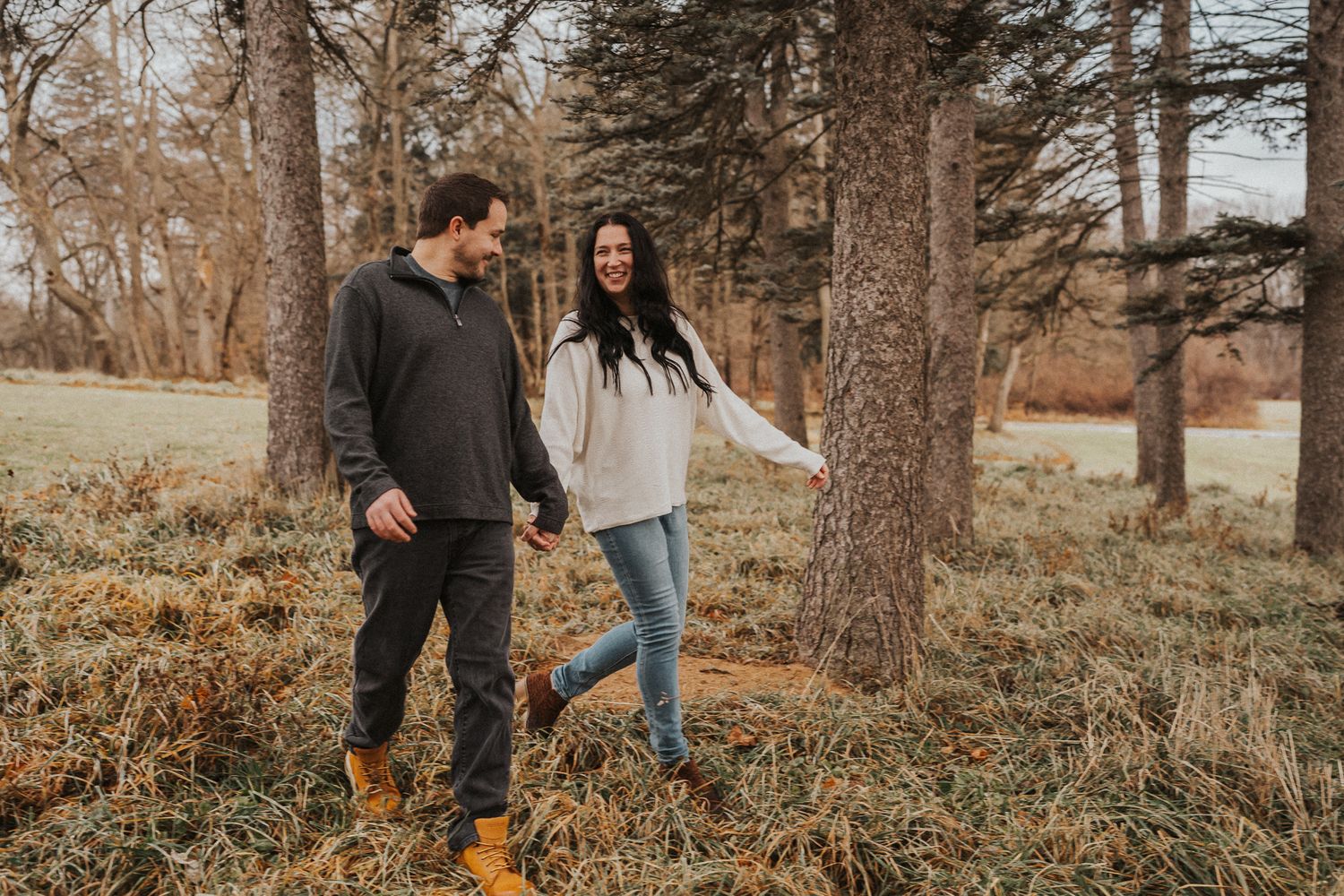Romantic couple walking through autumn forest setting in casual attire.