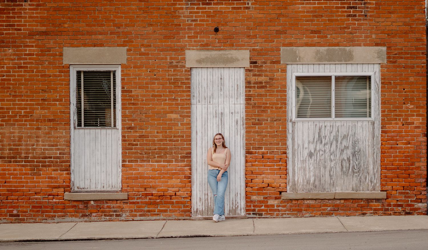 Series of artistic portraits against a rustic red brick wall with white framed windows.