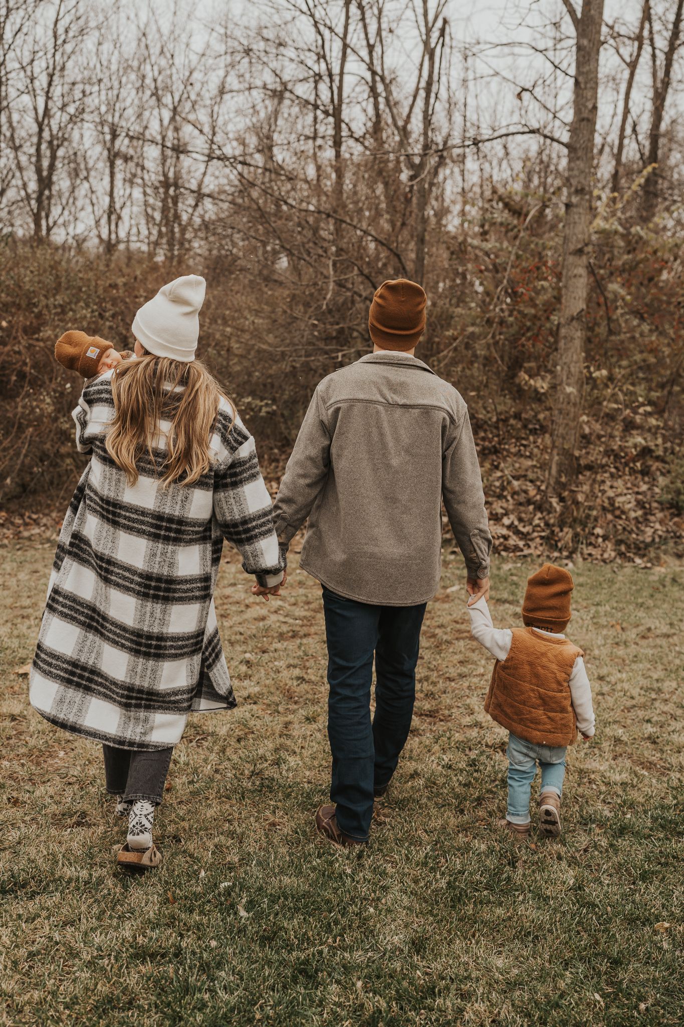 Family walking together in plaid and neutral outfits through autumn grass.