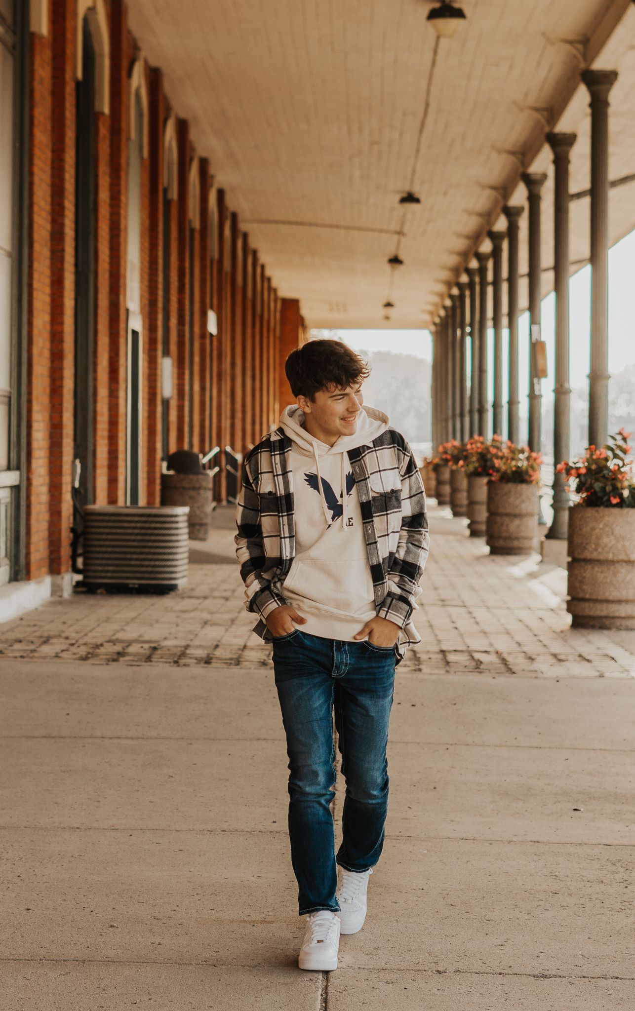 Person in plaid jacket walking through covered colonnade with decorative planters.