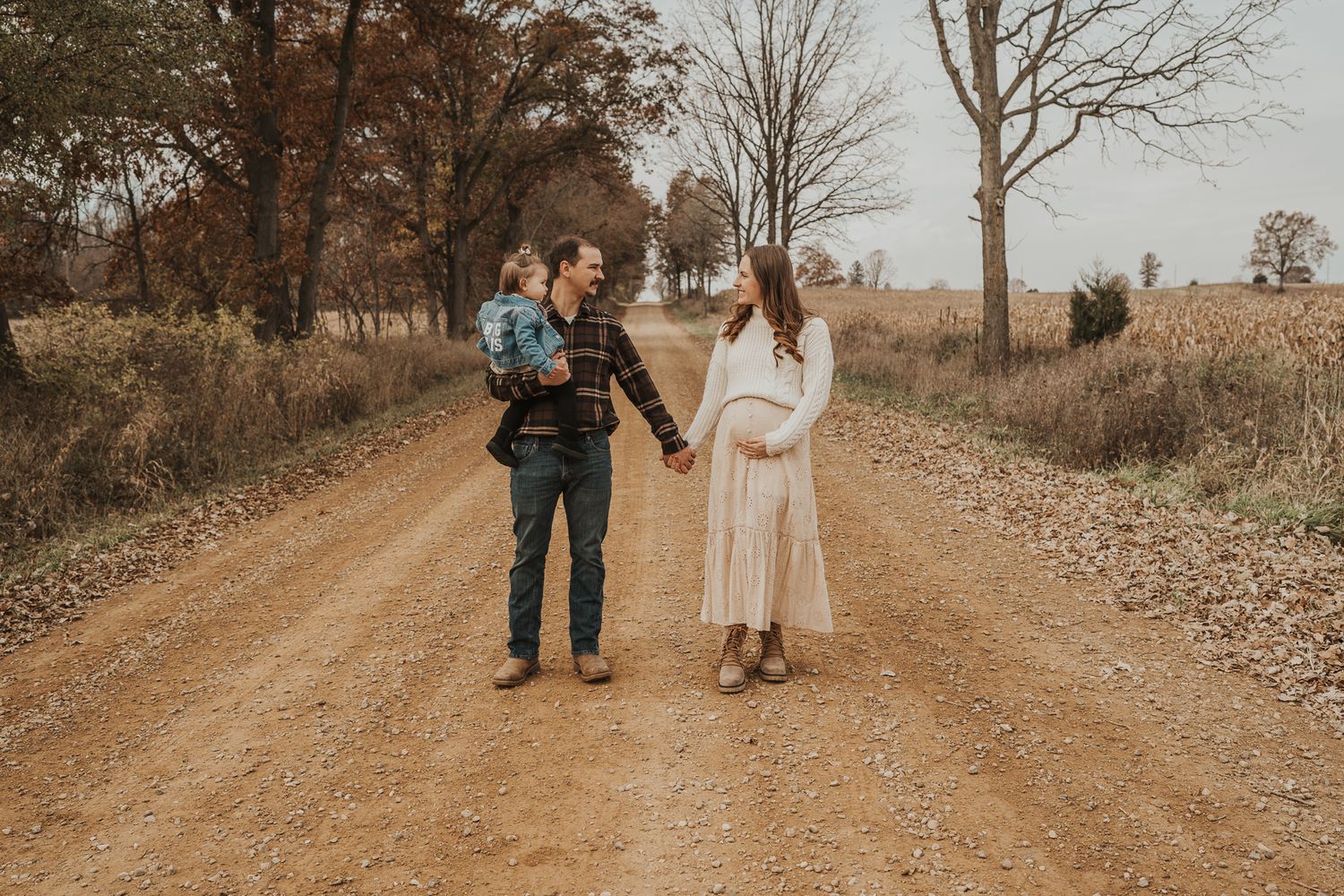 A couple walks hand in hand down a rustic dirt road during golden hour.