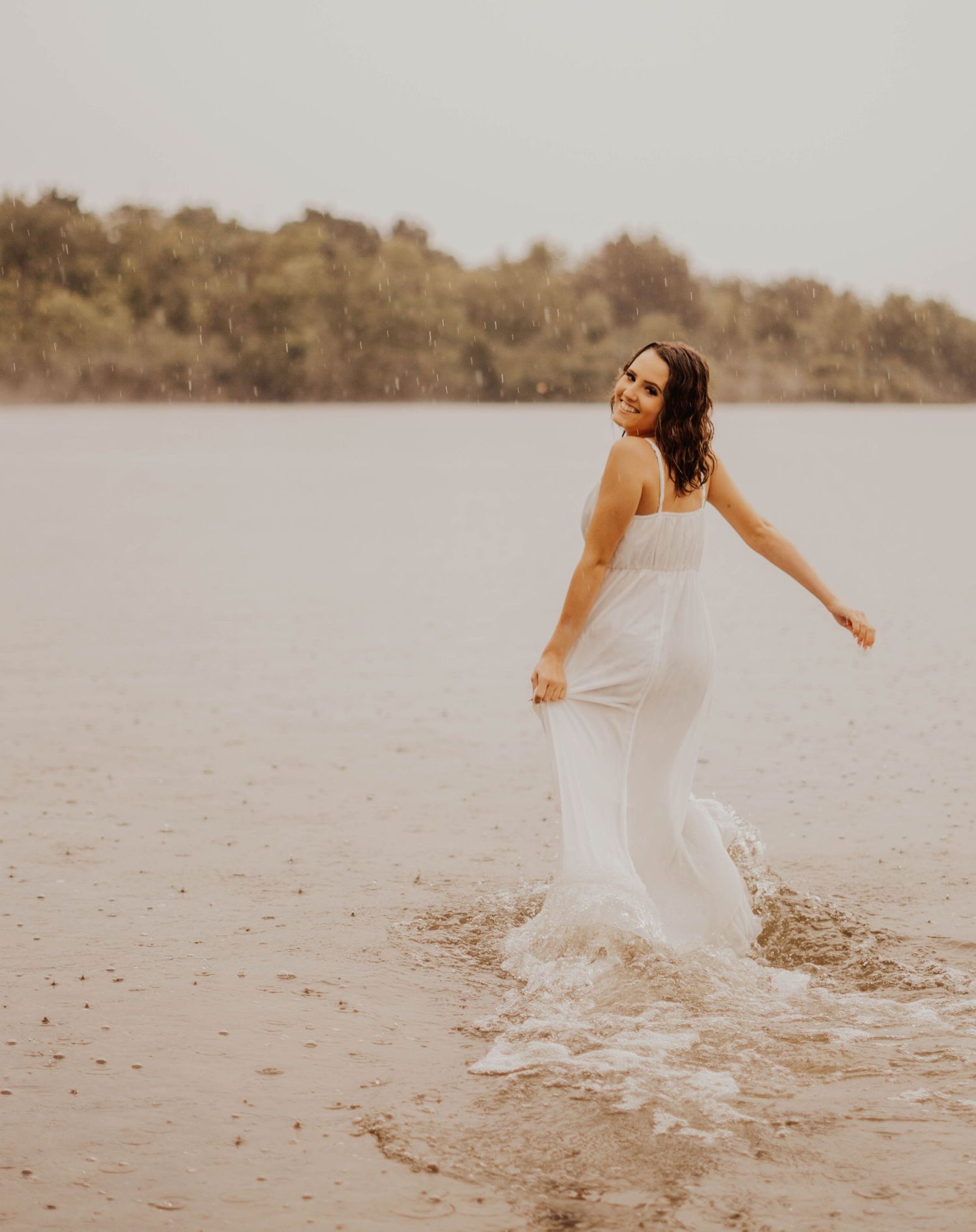 A flowing white dress twirls gracefully against a serene lakeside backdrop in warm sepia tones.