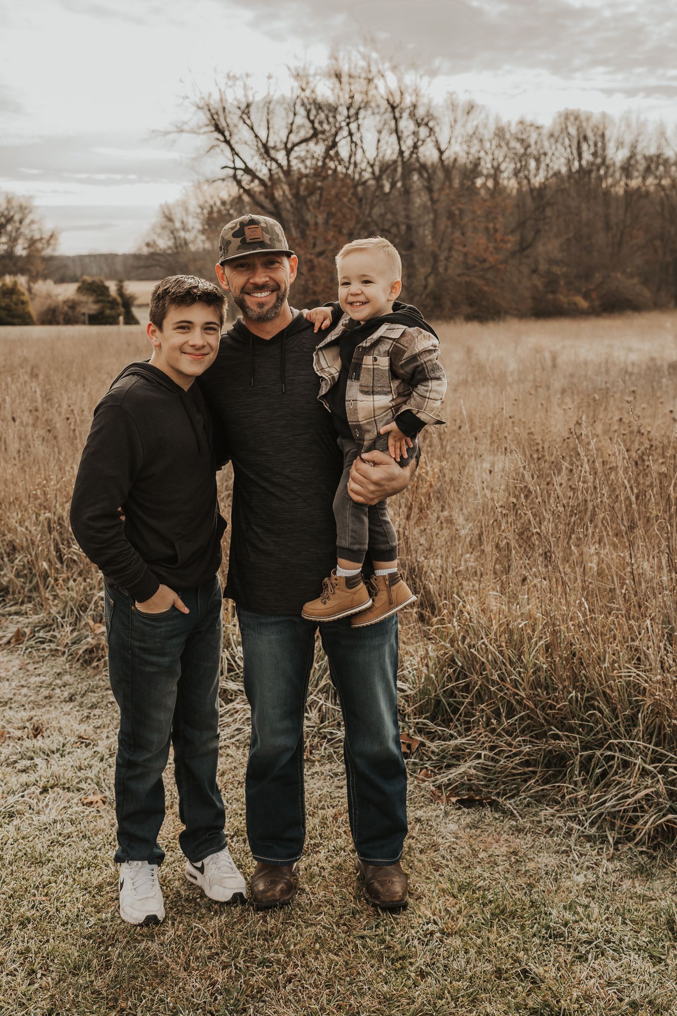 Three people stand together in casual dark clothing against a natural outdoor backdrop.