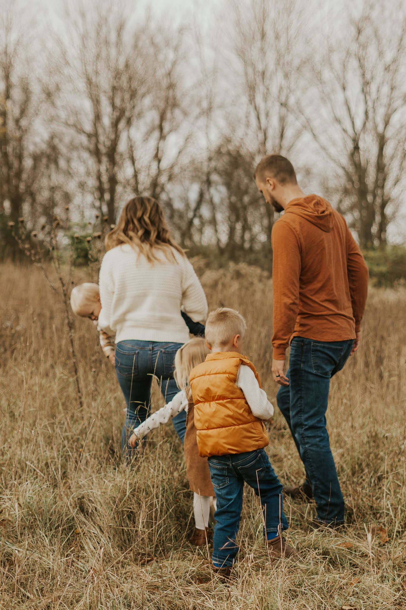 A family plays together in a field of tall grass on an autumn day.