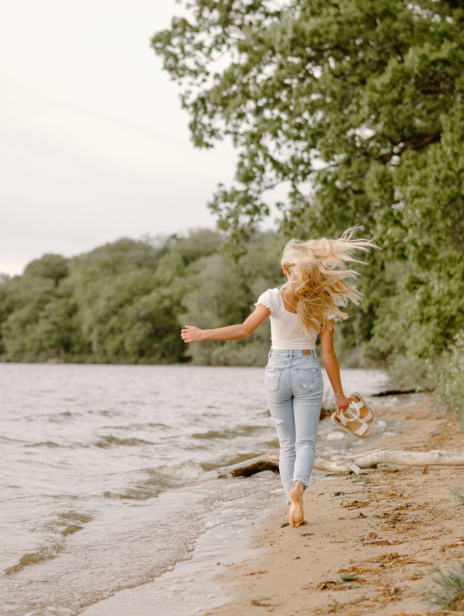 Senior photograph taken in jeans running playfully along a Michigan sandy beach shoreline.
