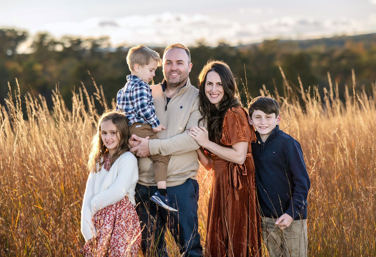 A loving family portrait set against a backdrop of golden autumn fields at sunset.