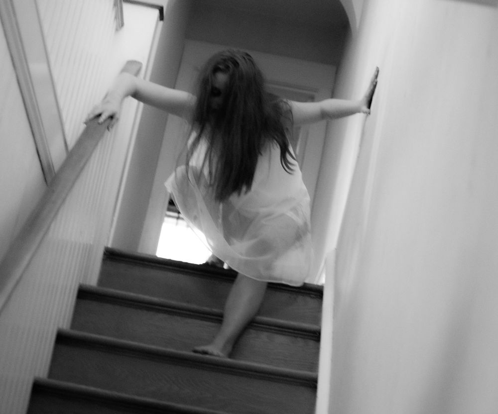 A figure in white descending stairs in a haunting black and white composition.