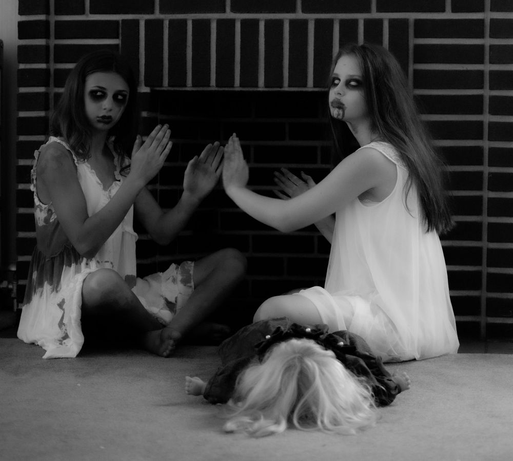 Two people in white dresses performing a dramatic scene against a brick wall.