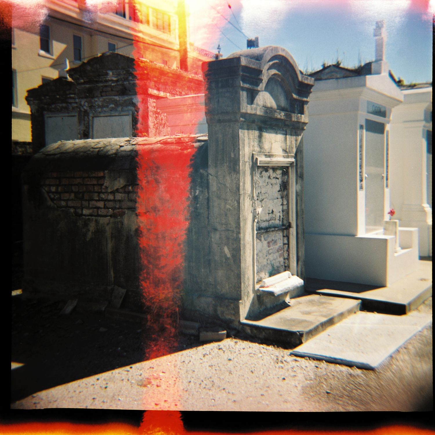 Historic cemetery with ornate stone tombs and mausoleums captured with light leak effect.