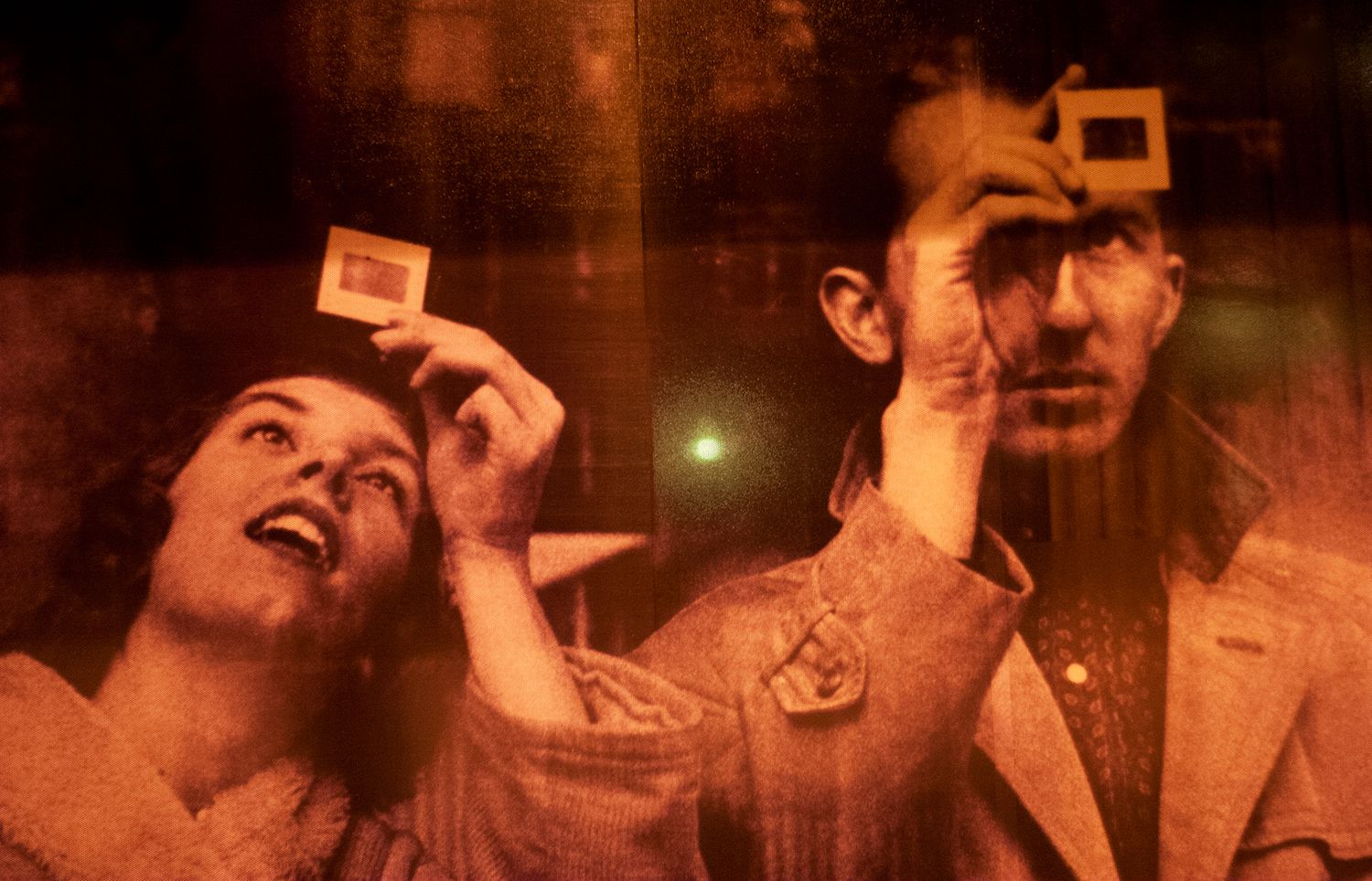 A vintage-toned photo shows people holding up film negatives against warm backlighting.