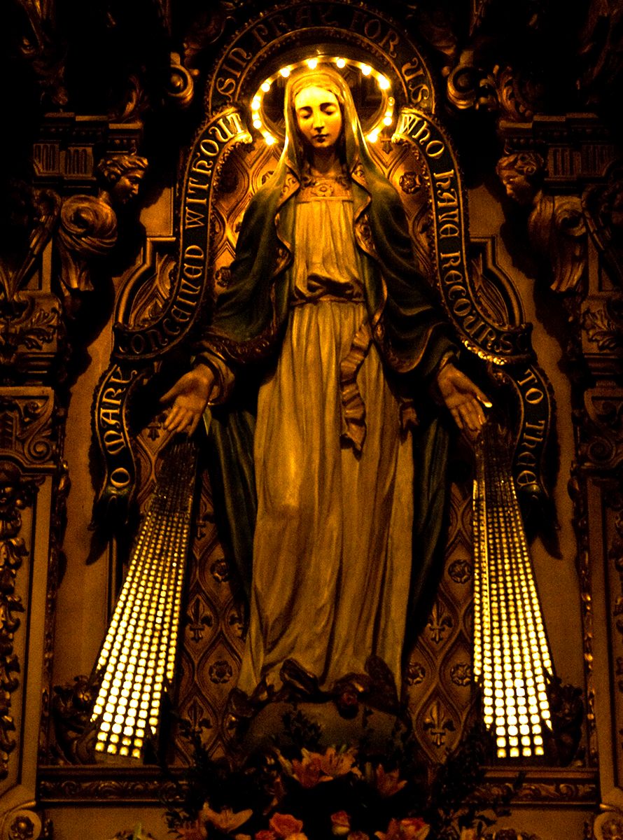 Ornate golden religious statue in Gothic cathedral setting with dramatic lighting.
